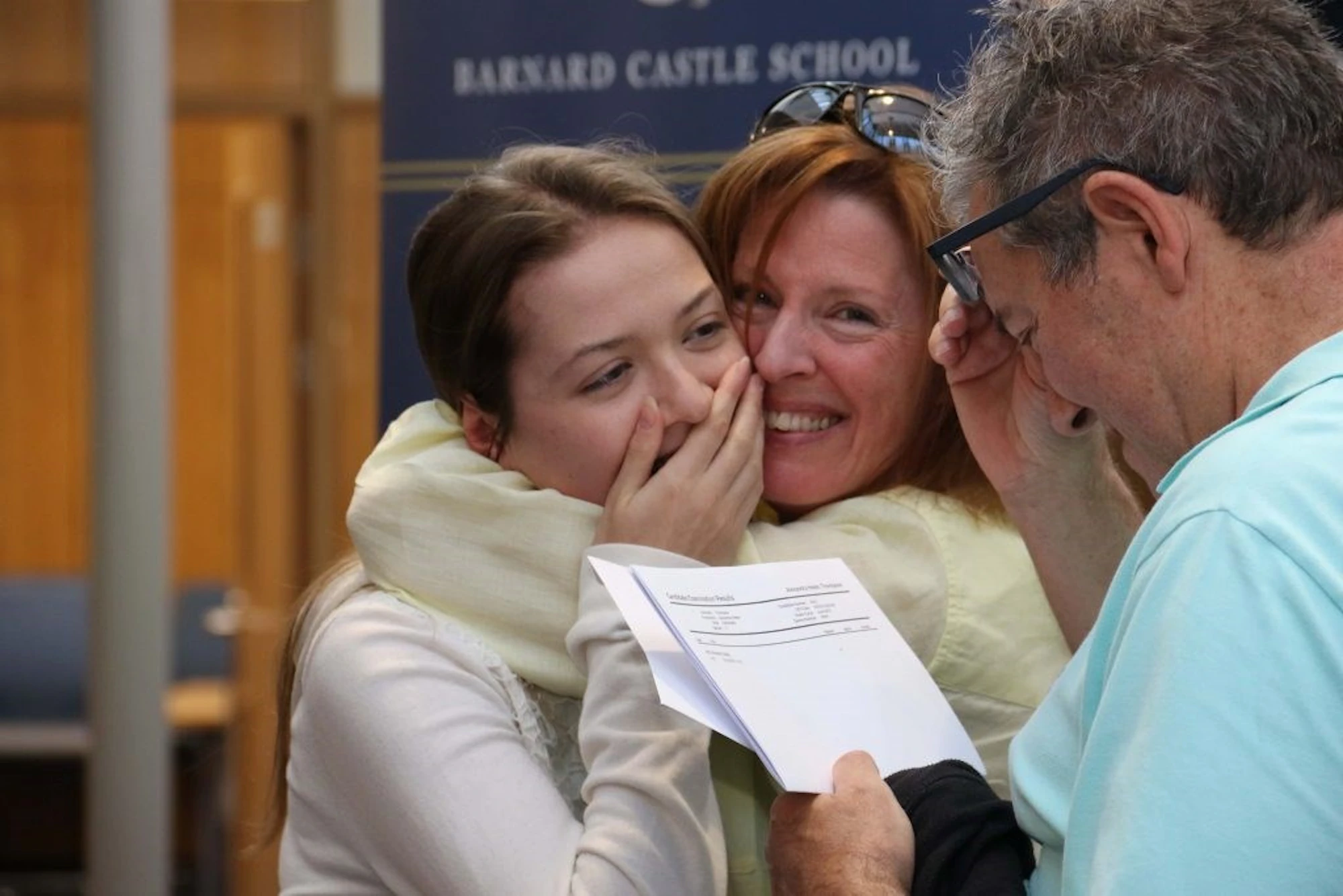 Barnard Castle School pupil hugging her mother while her father reads her results, all smiling,