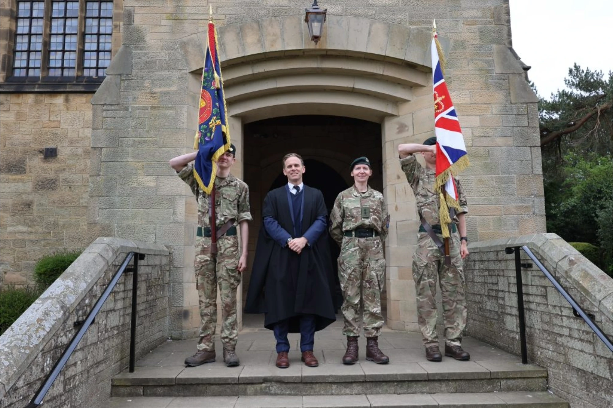 VE Day 80 Headmaster's Assembly. Headmaster, David Creswell, accompanied by three individuals in military uniform, holding military flags.