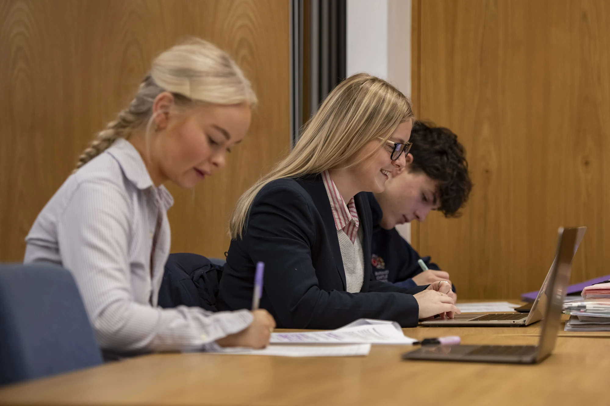 Barnard Castle School Sixth Formers working at a desk with their laptops and writing notes in a classroom.