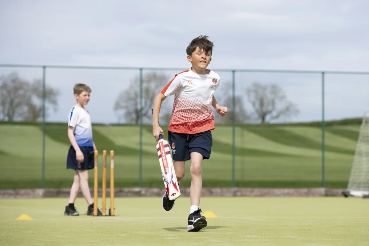 Two Barnard Castle School pupils playing cricket on a grassy field, focused on the game with a bat and ball in hand.
