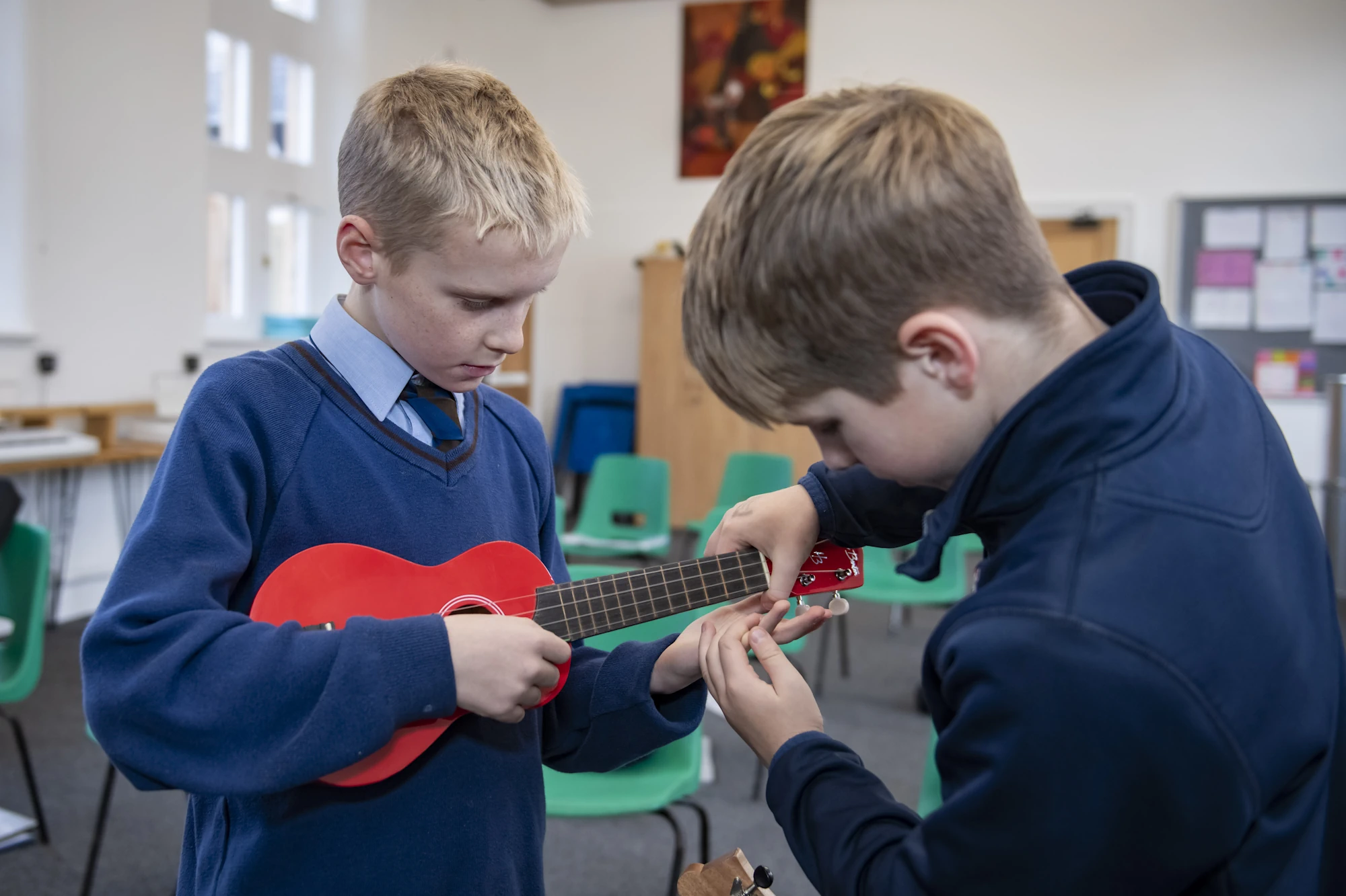 Two Barnard Castle School pupils playing ukuleles together in a bright classroom, one helping the other with chords.