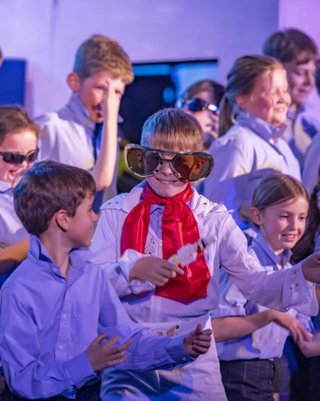 Barnard Castle School pupils in a production, one of them smiling with big glasses and an Elvis outfit.