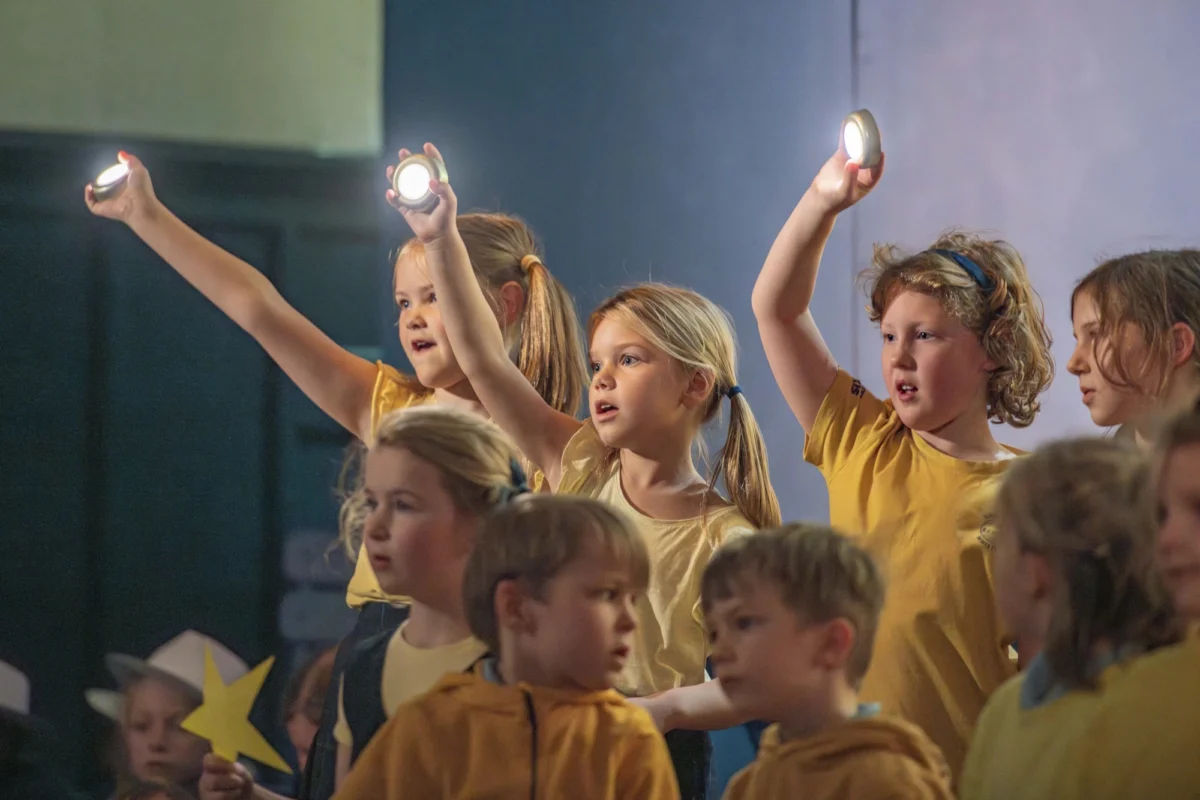Barnard Castle School pupils singing and holding lights on stage in a school production.