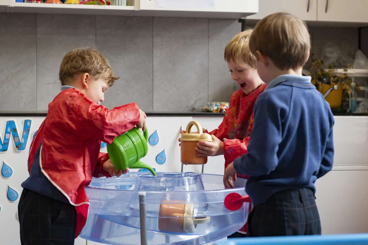 Three Barnard Castle Students partaking in enriching activities involving water and buckets in a classroom.