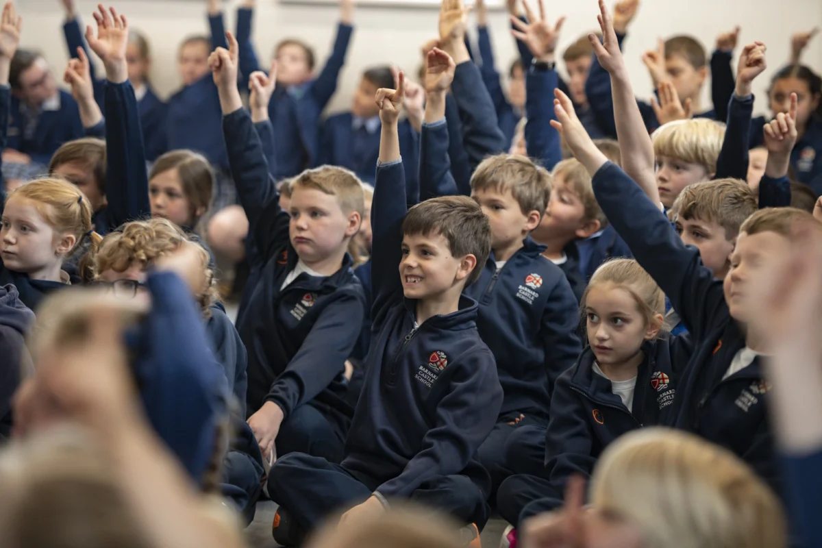 Barnard Castle School pupils raising their hands, eager to participate in an assembly.
