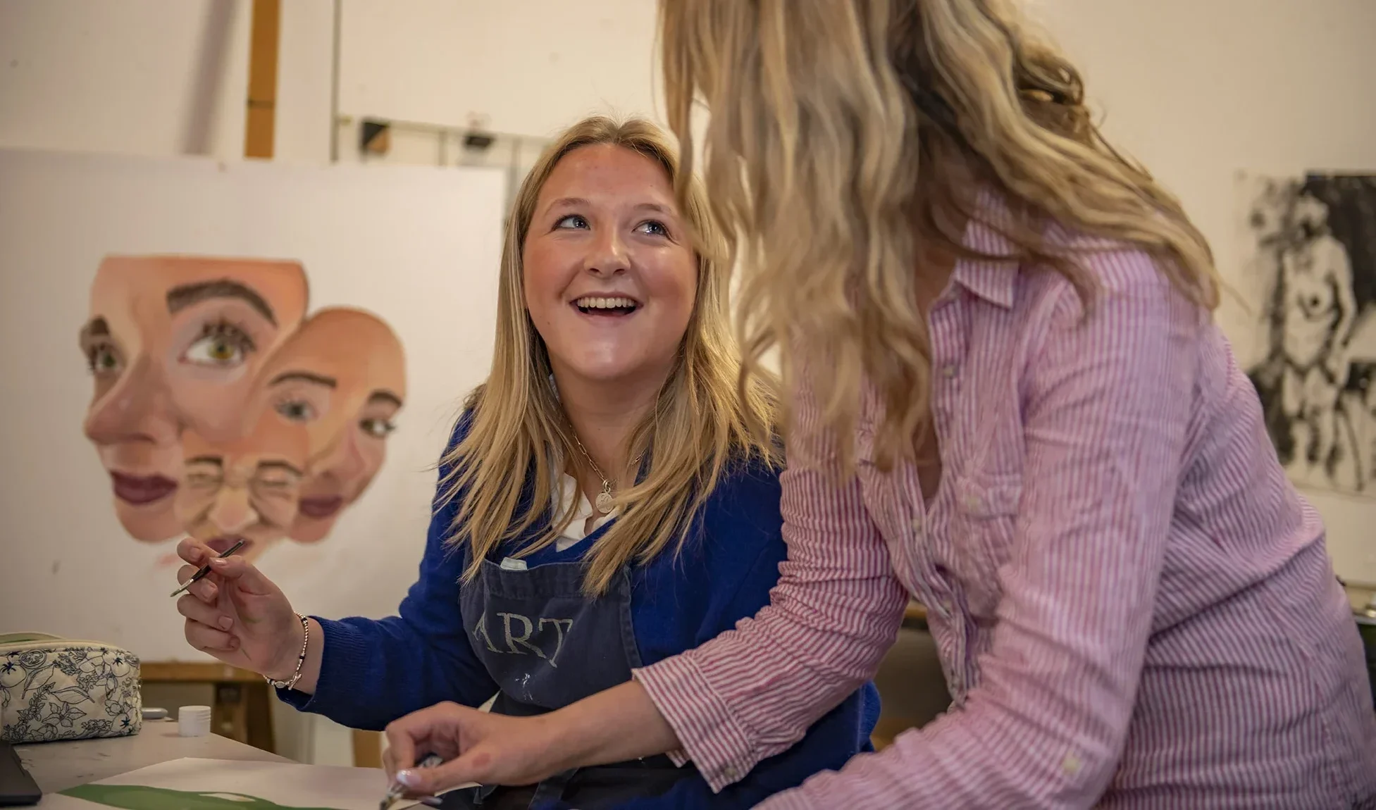 A Barnard Castle School art student and teacher laugh together while painting on paper, enjoying a creative and joyful moment.