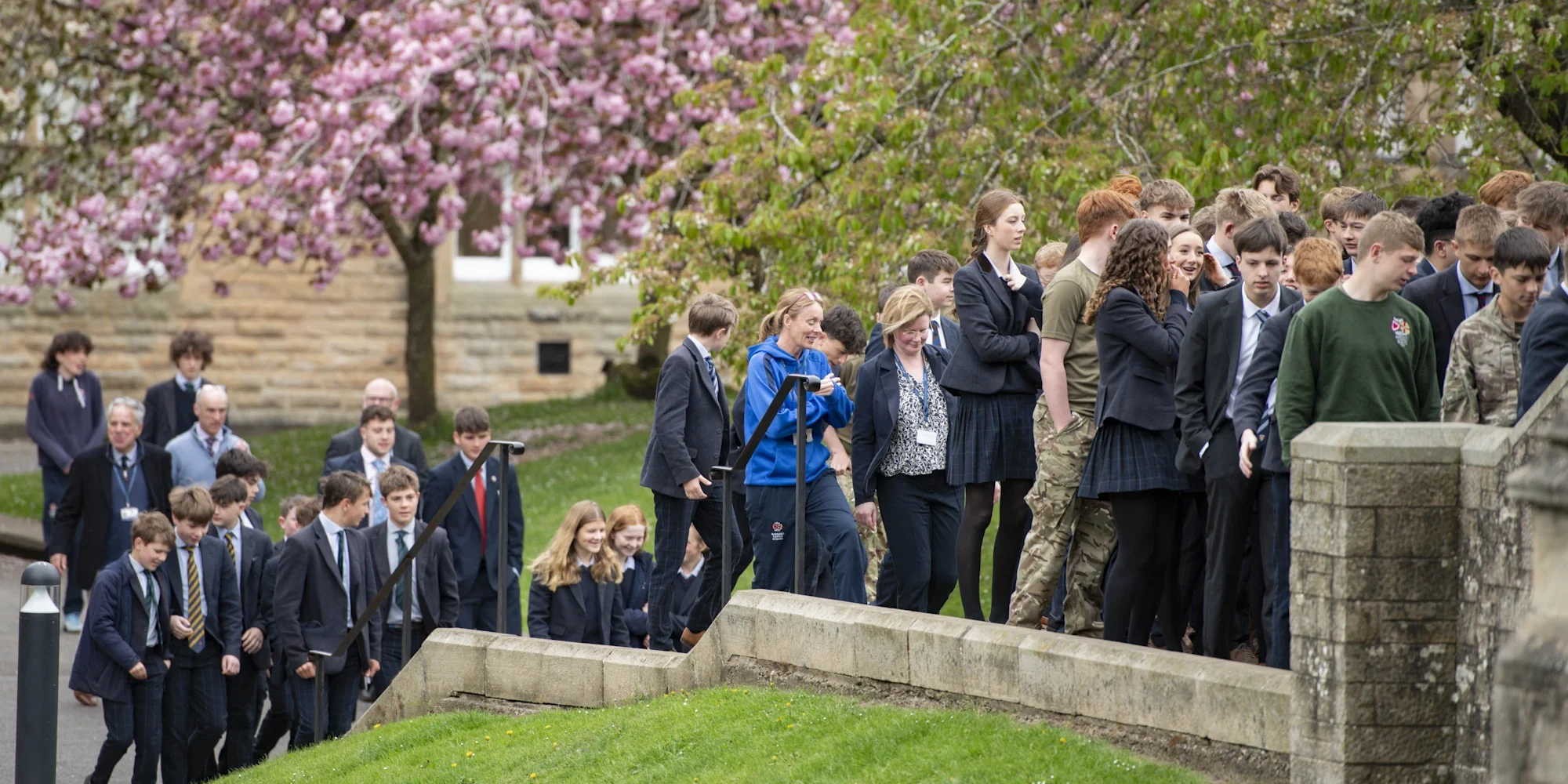 A group of students walks up the steps of Barnard Castle School campus, smiling and engaging with one another.