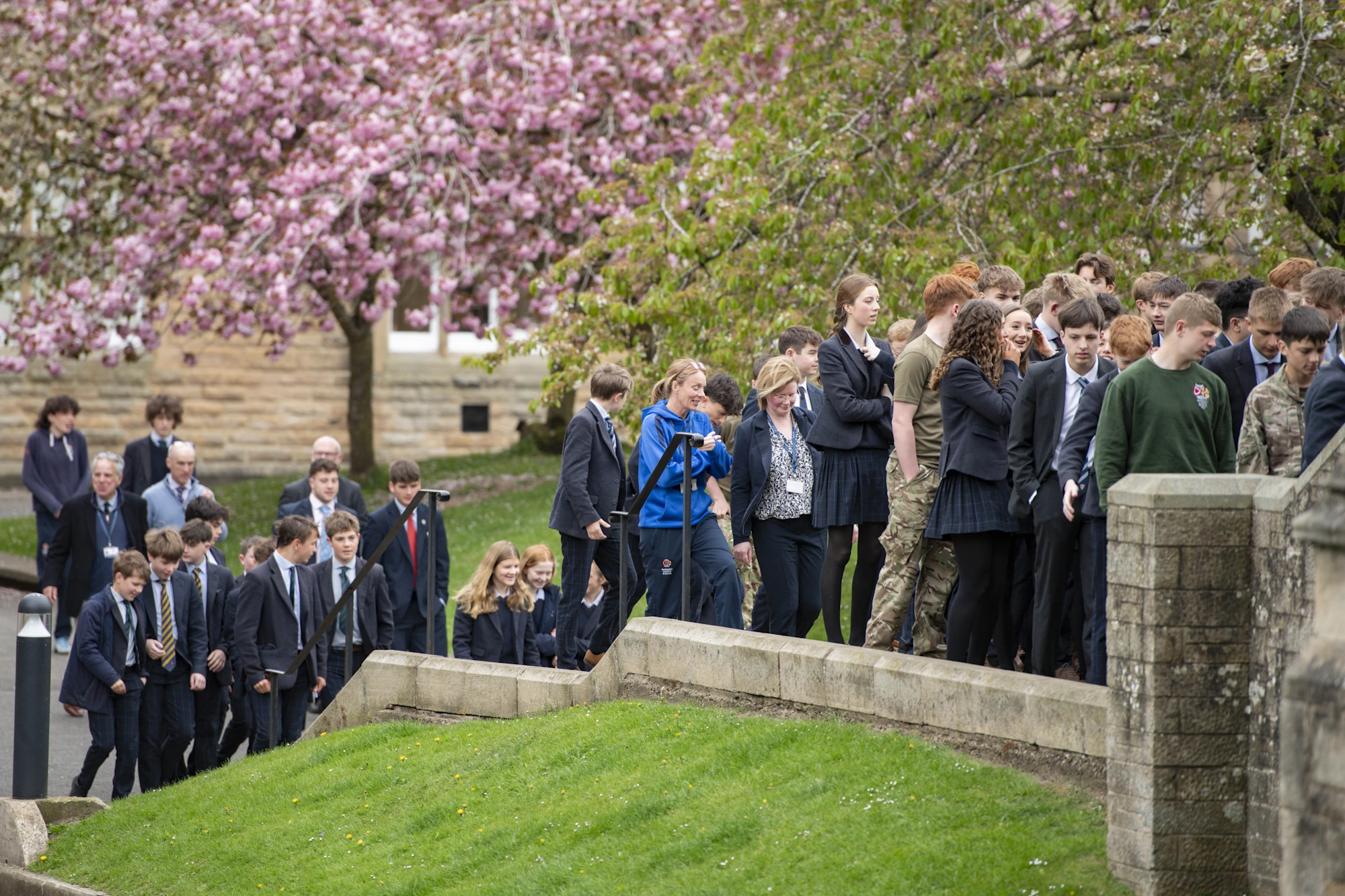 A group of students walks up the steps of Barnard Castle School campus, smiling and engaging with one another.