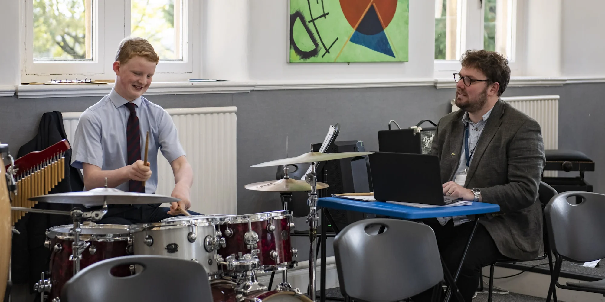 Barnard Castle School pupil playing the drums with a teacher watching.