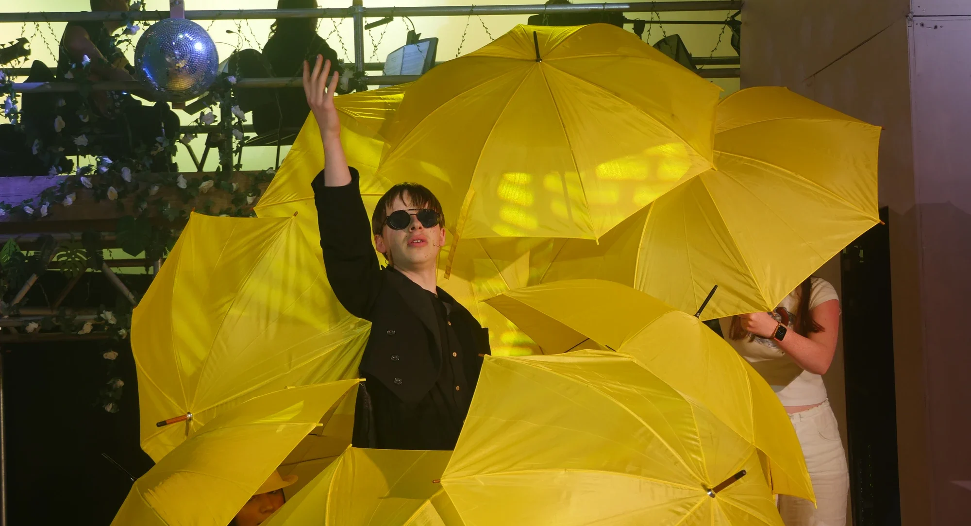 Senior school student performing on stage surrounded by yellow umbrellas.