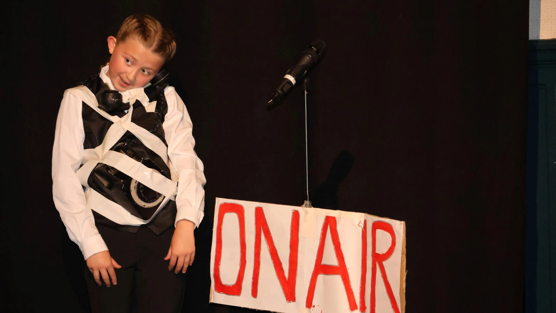 A student tied to a sign that reads 'On Air'.