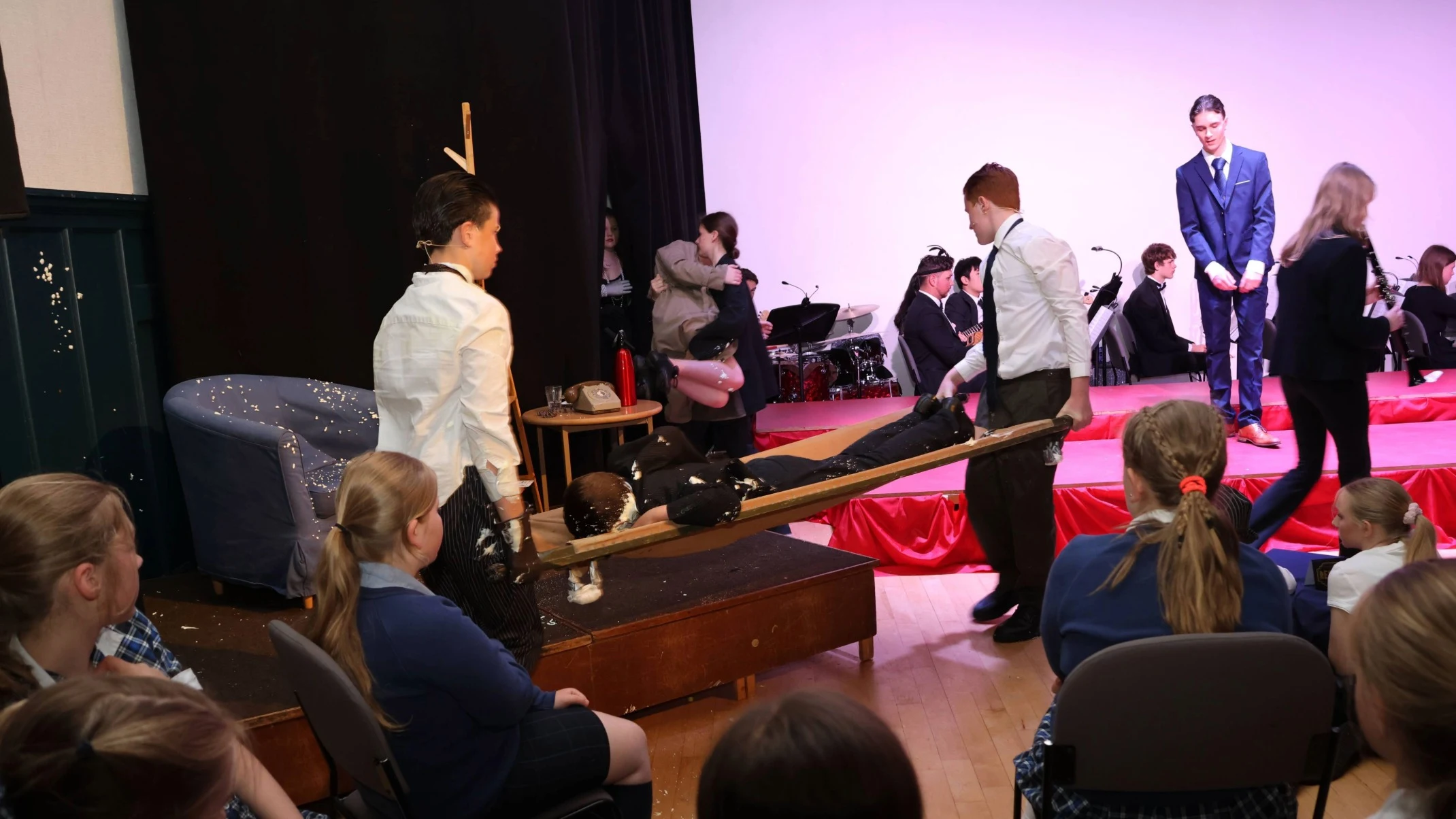 A student is carried out on a prop stretcher during a performance of Bugsy Malone.