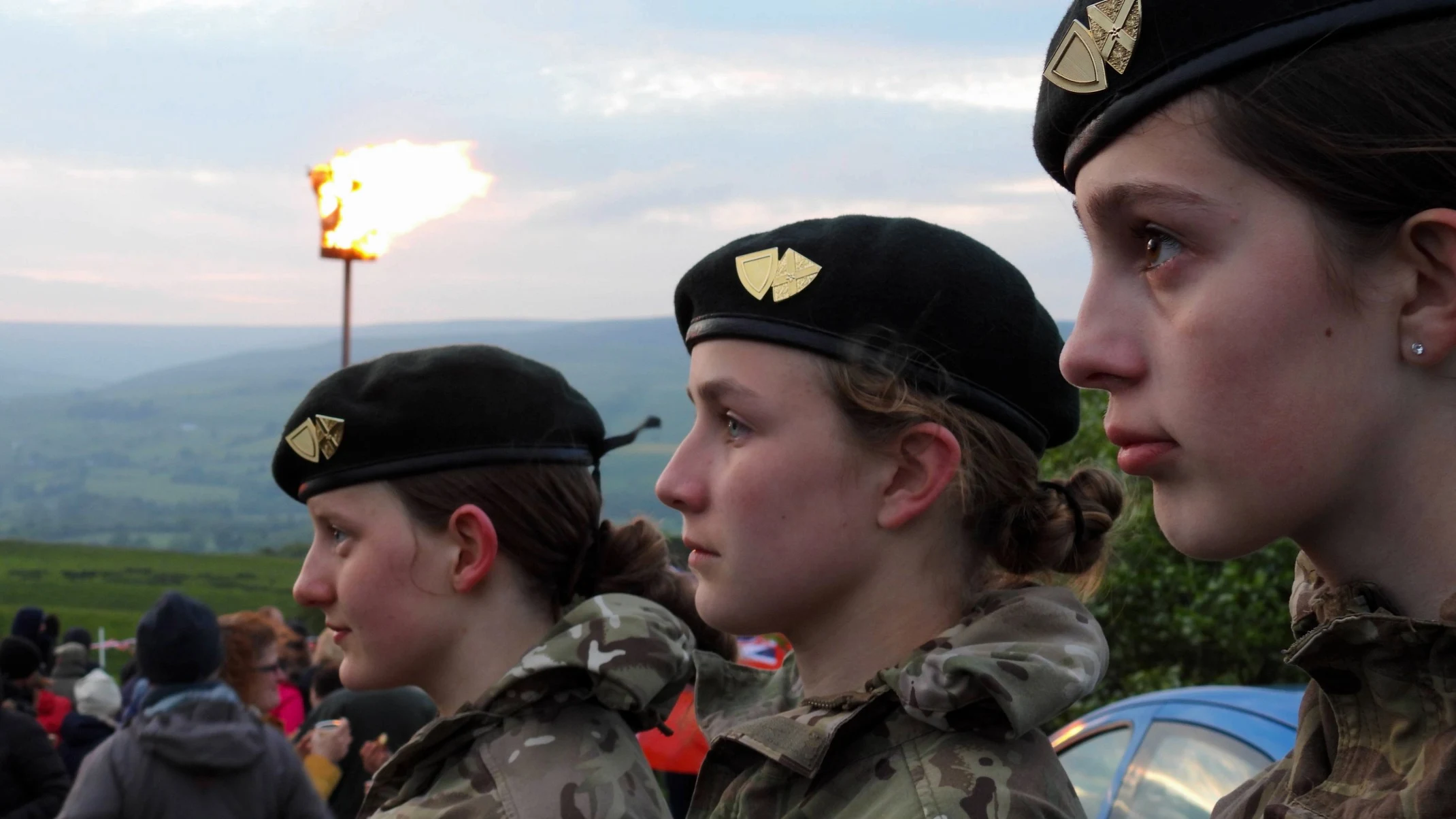 Three young people in military uniform in front of a burning beacon.