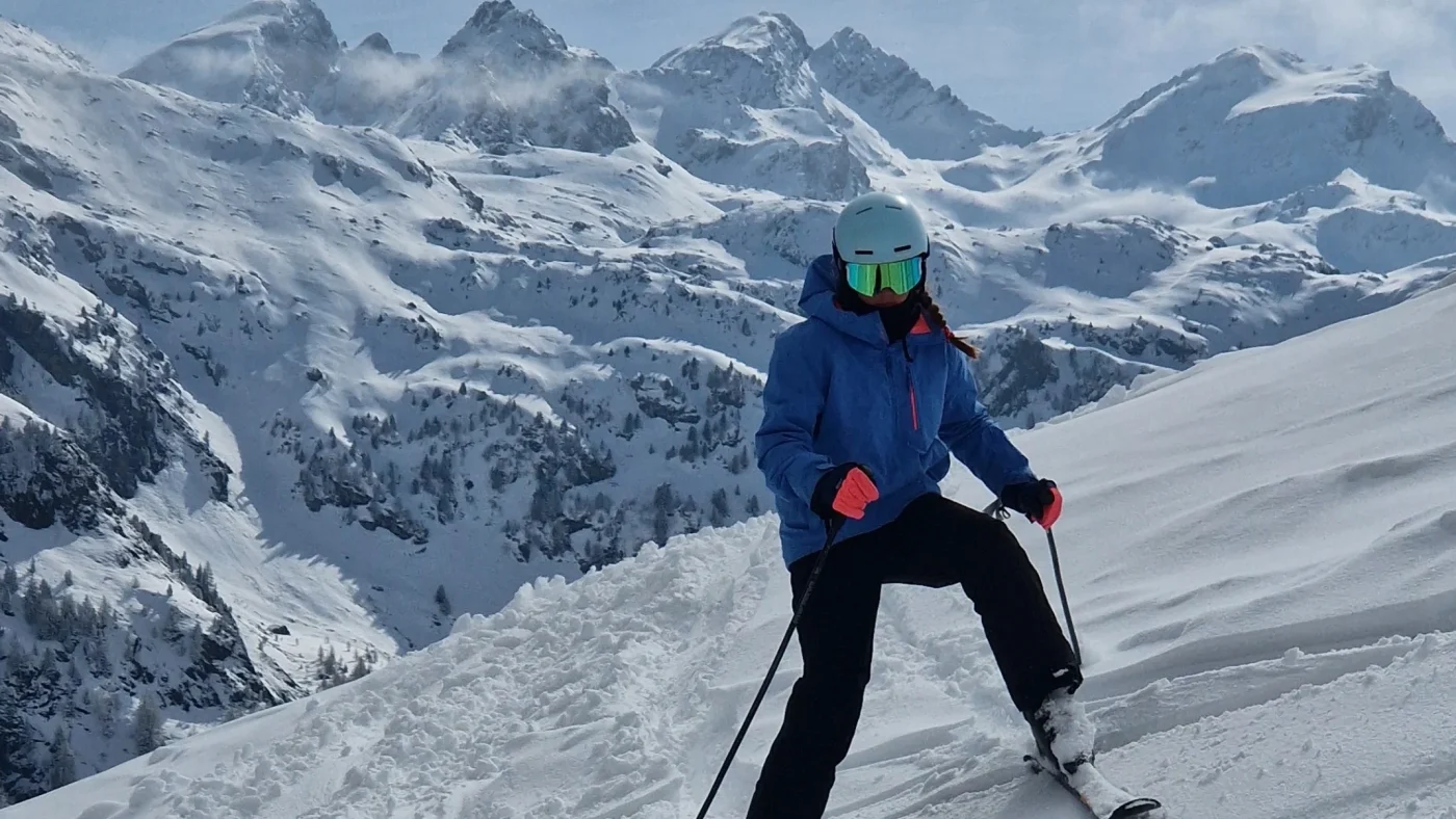 A Barney student poses with their skis in front of a mountain range.