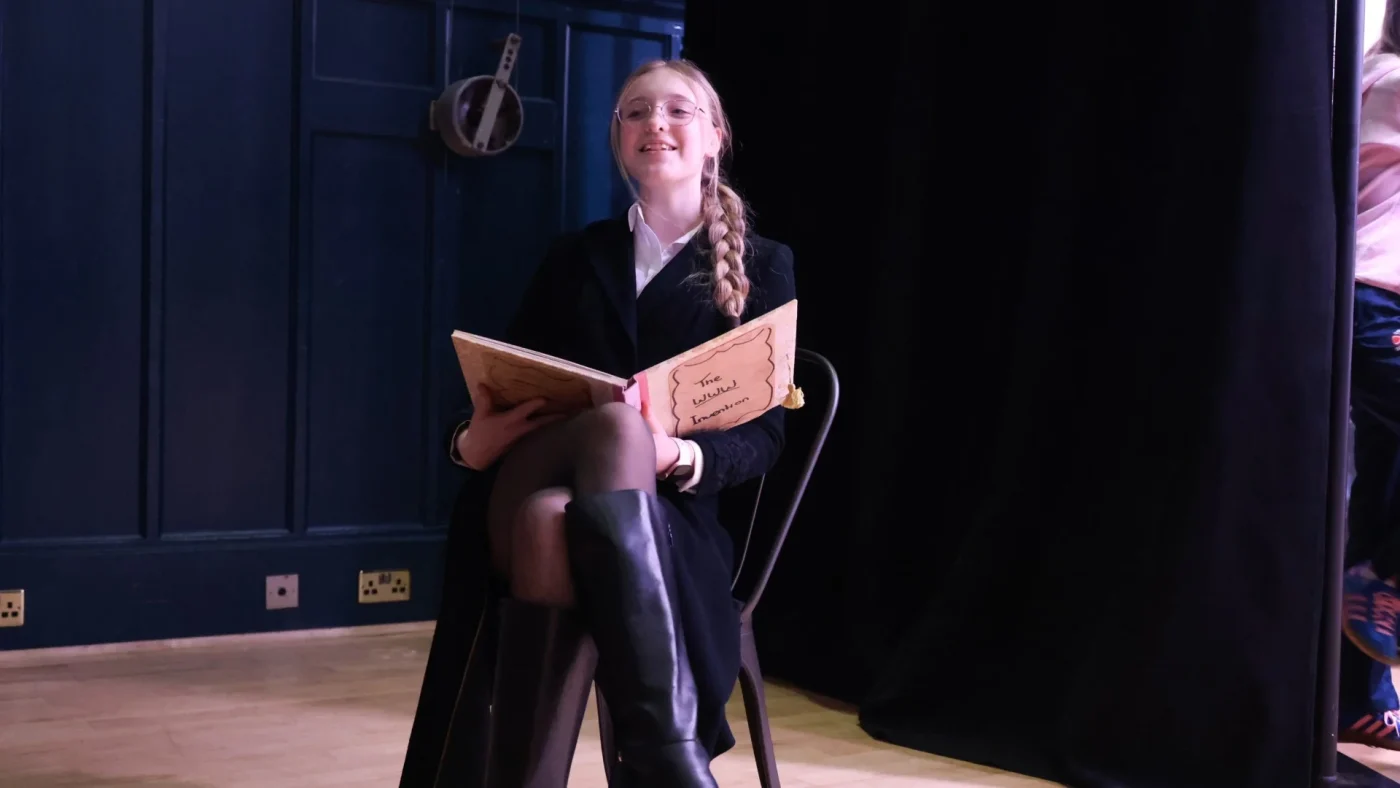 A Barney student sitting in a chair holding a book whose cover reads 'WWW invention'.