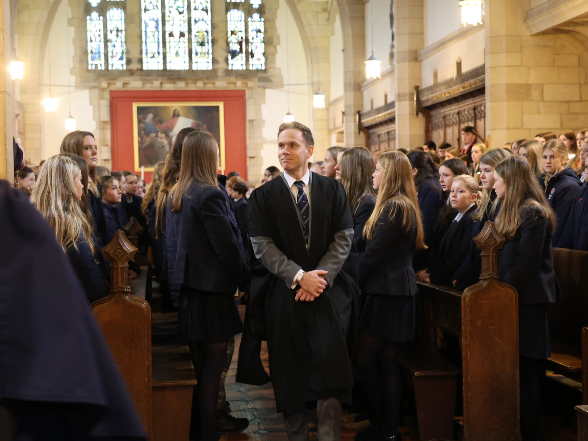 Headmaster walking down aisle in assembly, with pupils standing either side.