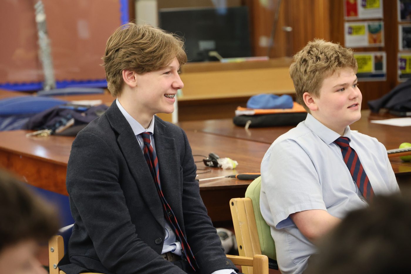 Two students in school uniform sit side by side, smiling and listening during a session.