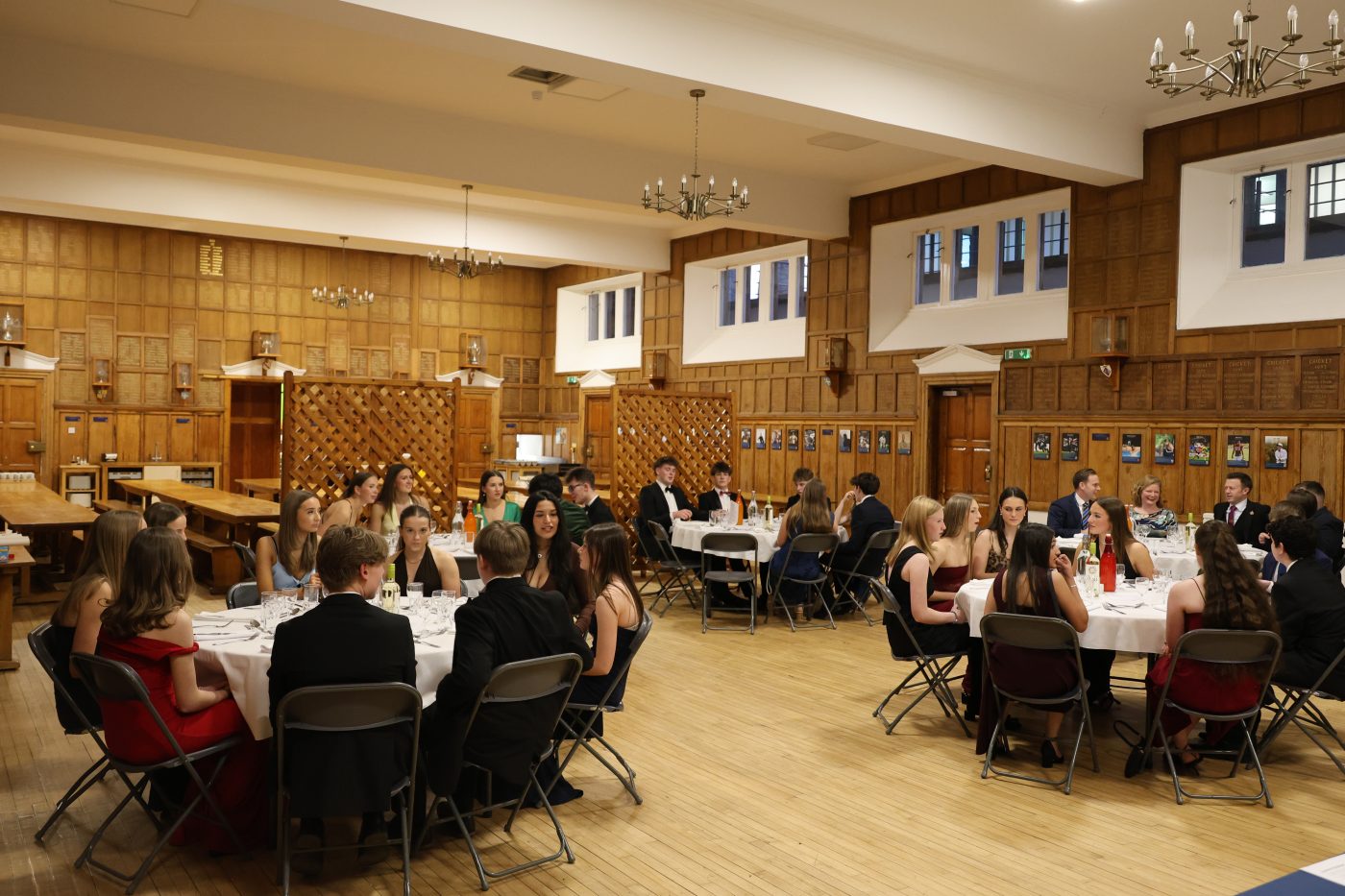 Students dressed formally sit at round tables in a large hall, attending a dinner event.
