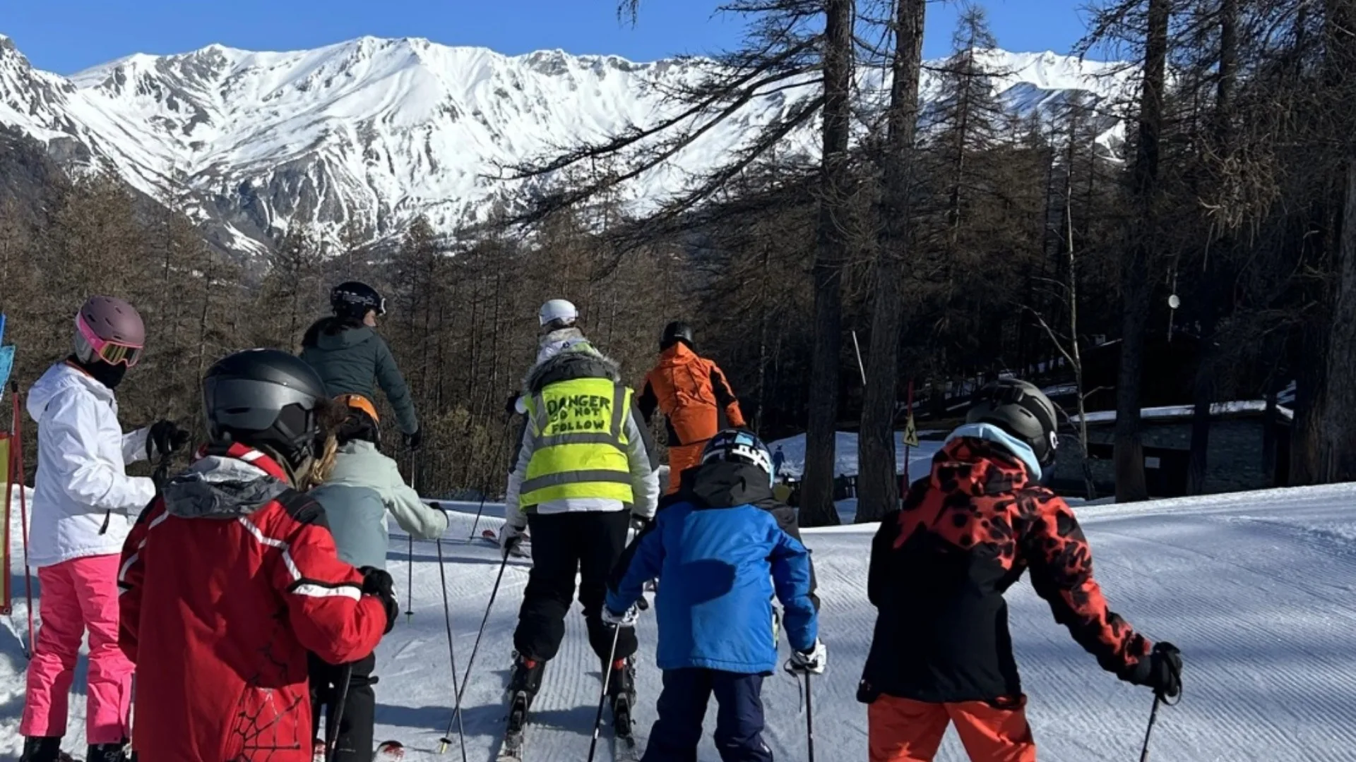A group of Barney students skiing against a mountain range with blue skies.