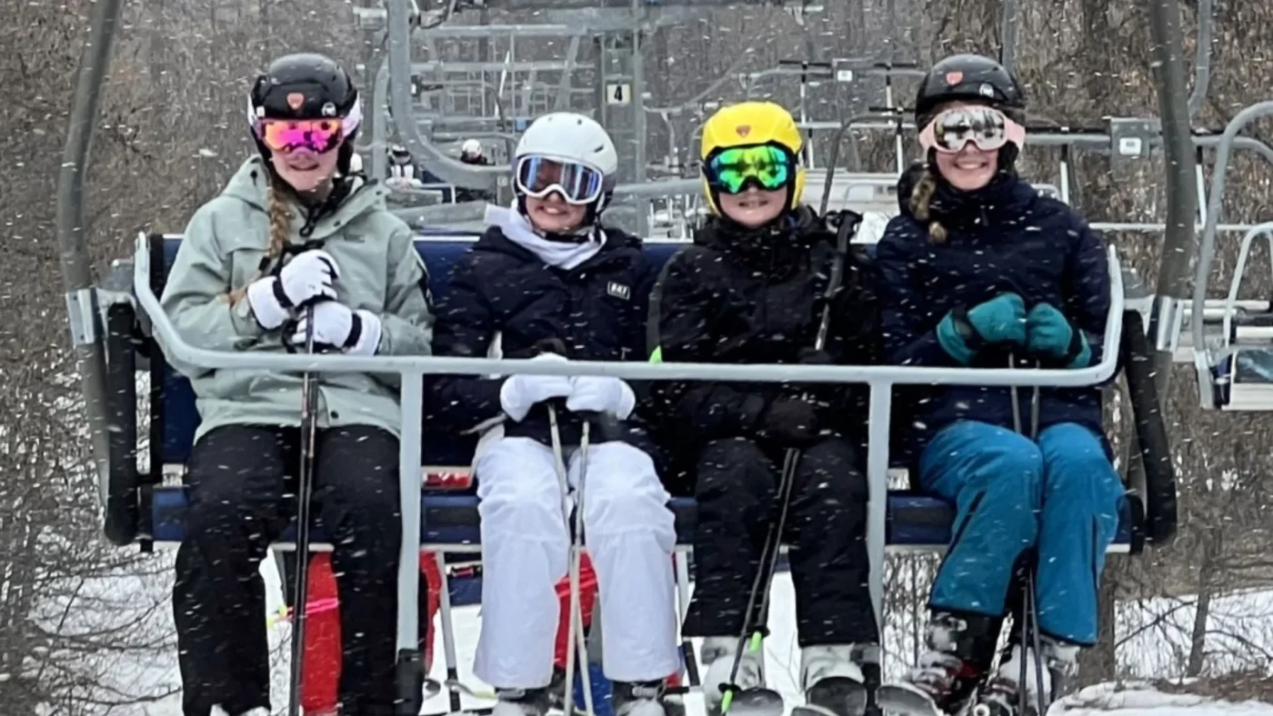 Four Barney students sitting on a ski lift in the snow.