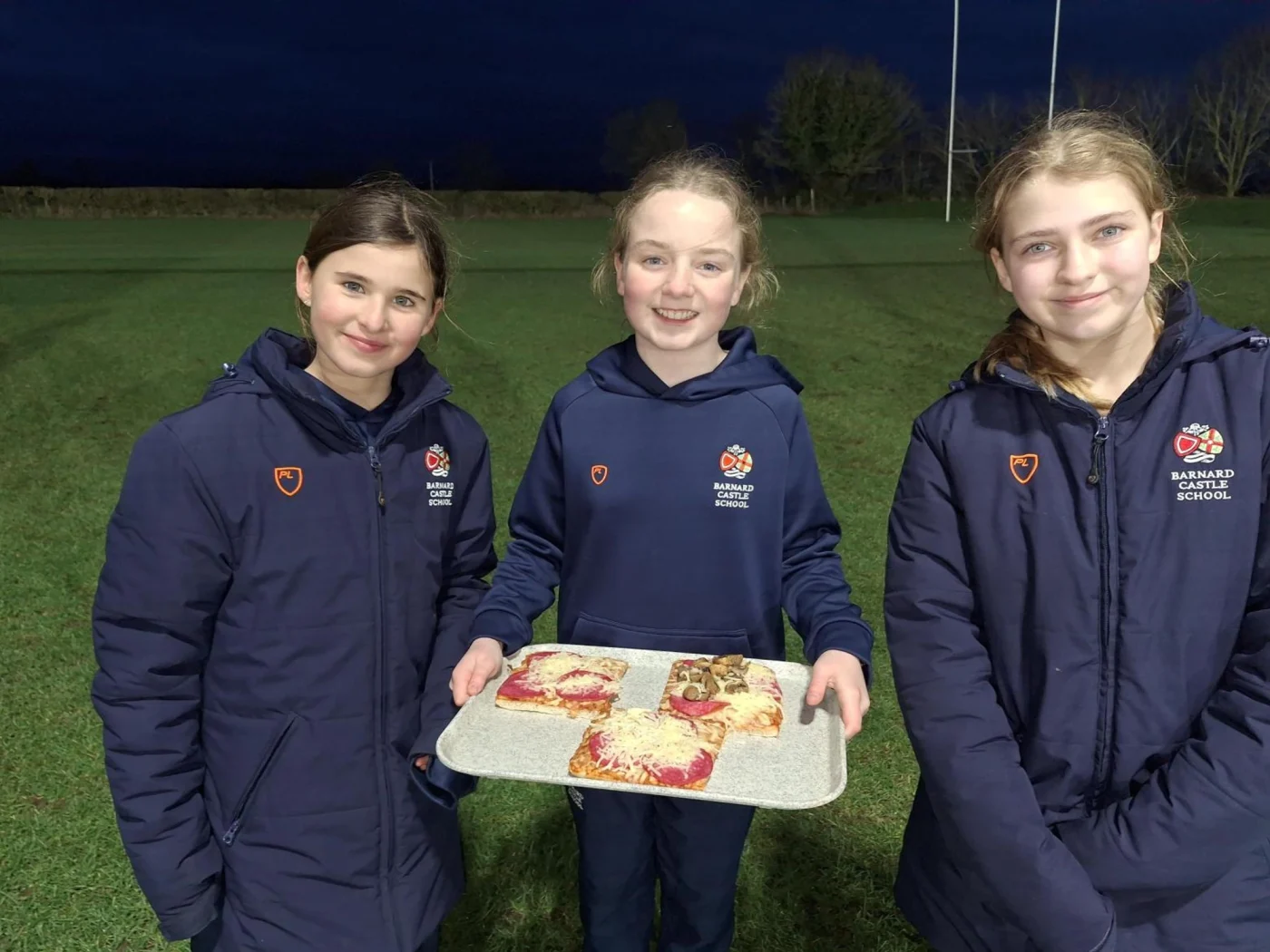 Three Barney pupils smiling with pizza during the Great Tommy Sleep Out.
