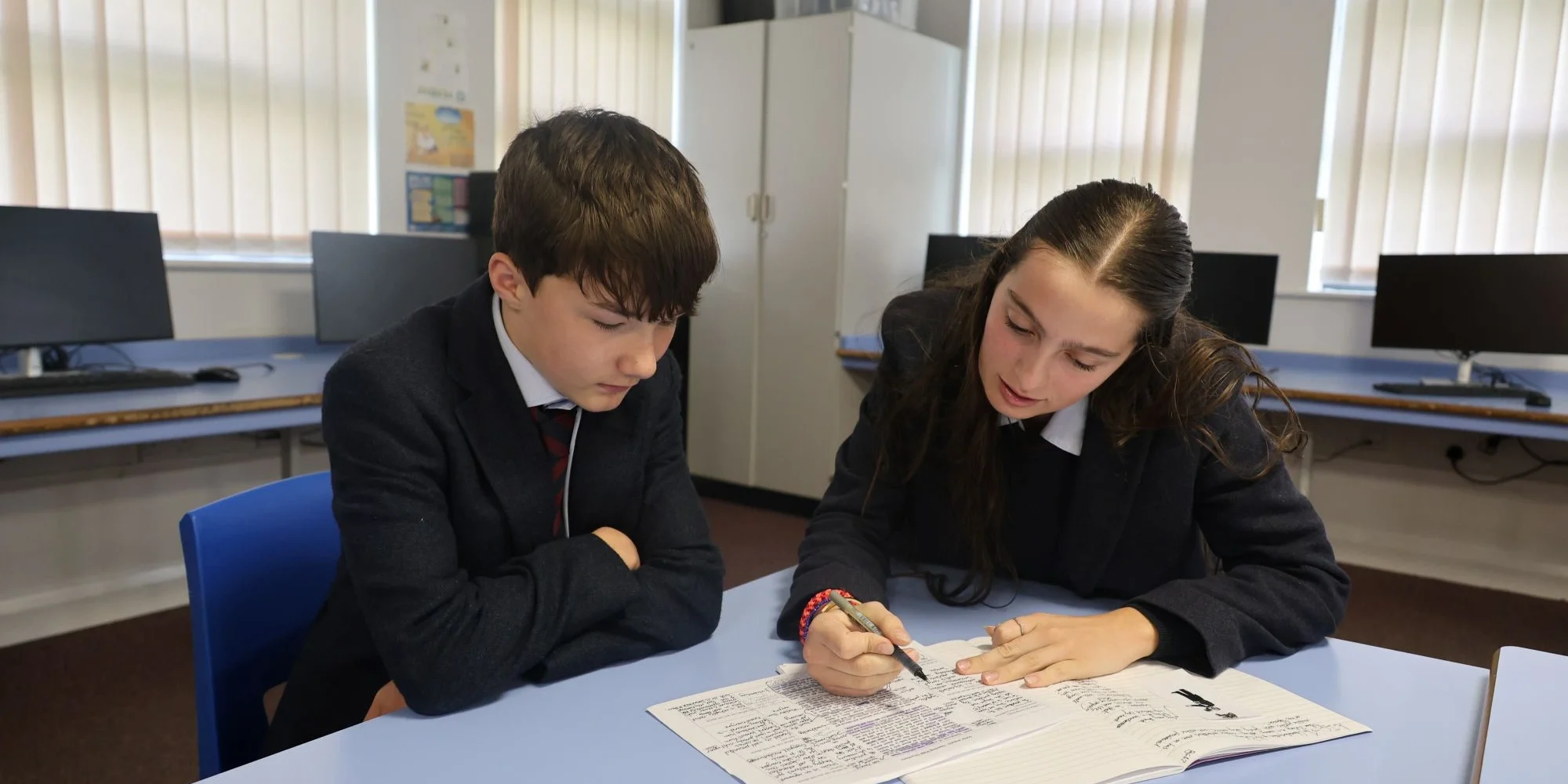 Two Barnard Castle students in school uniforms work closely together on an assignment in a bright, modern classroom.