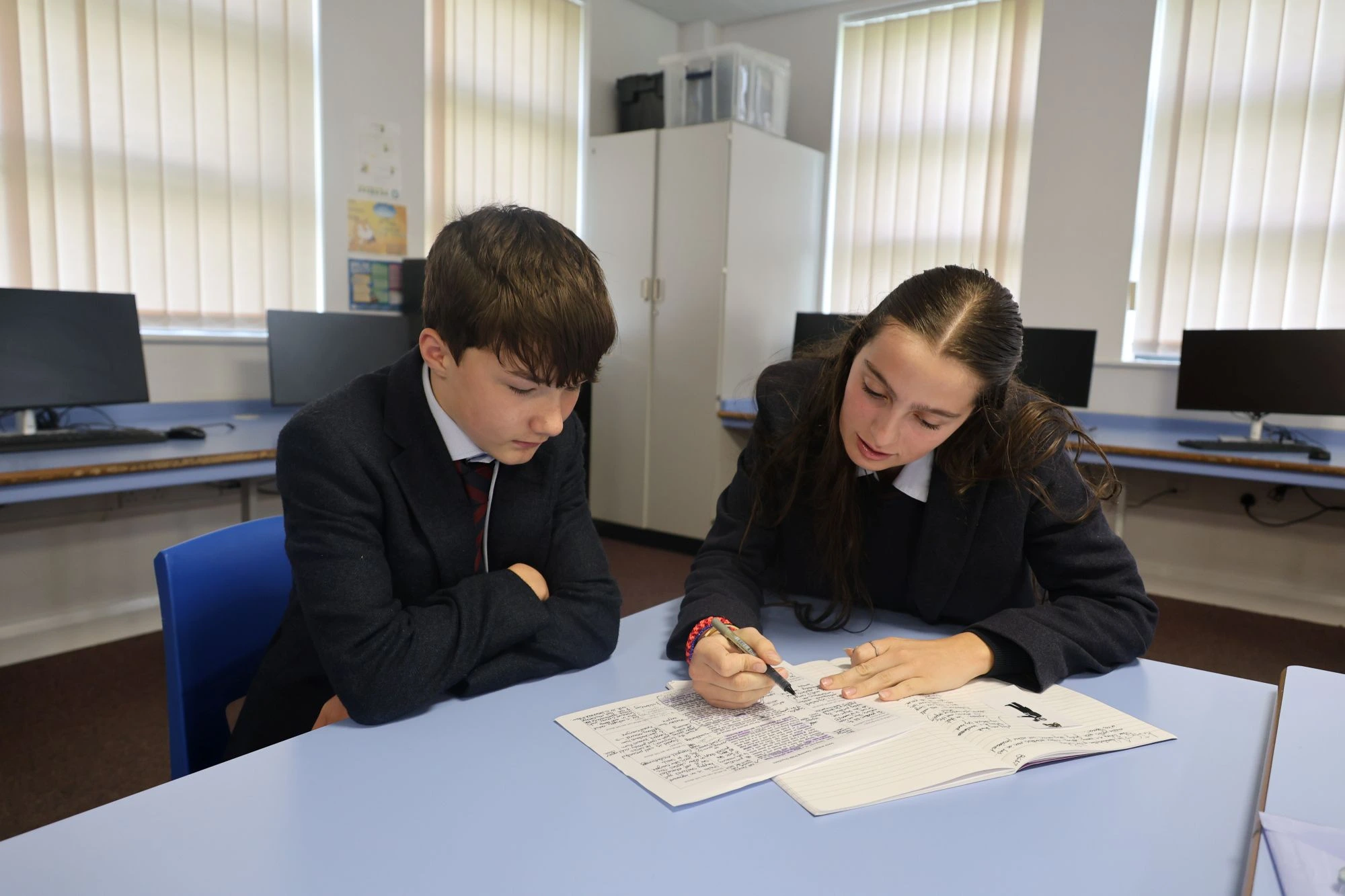Two Barnard Castle students in school uniforms work closely together on an assignment in a bright, modern classroom.