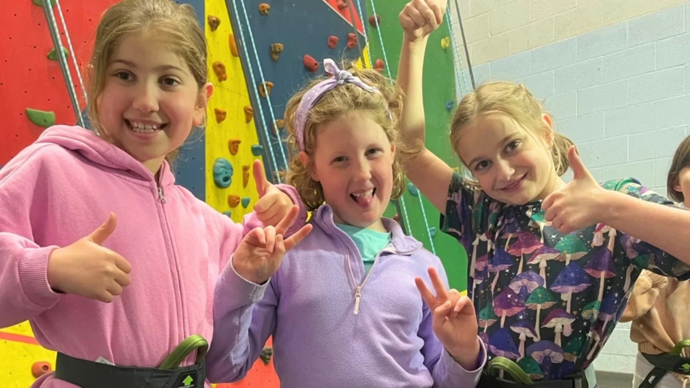 Year 4 Barney students posing in front of a colourful climbing wall.