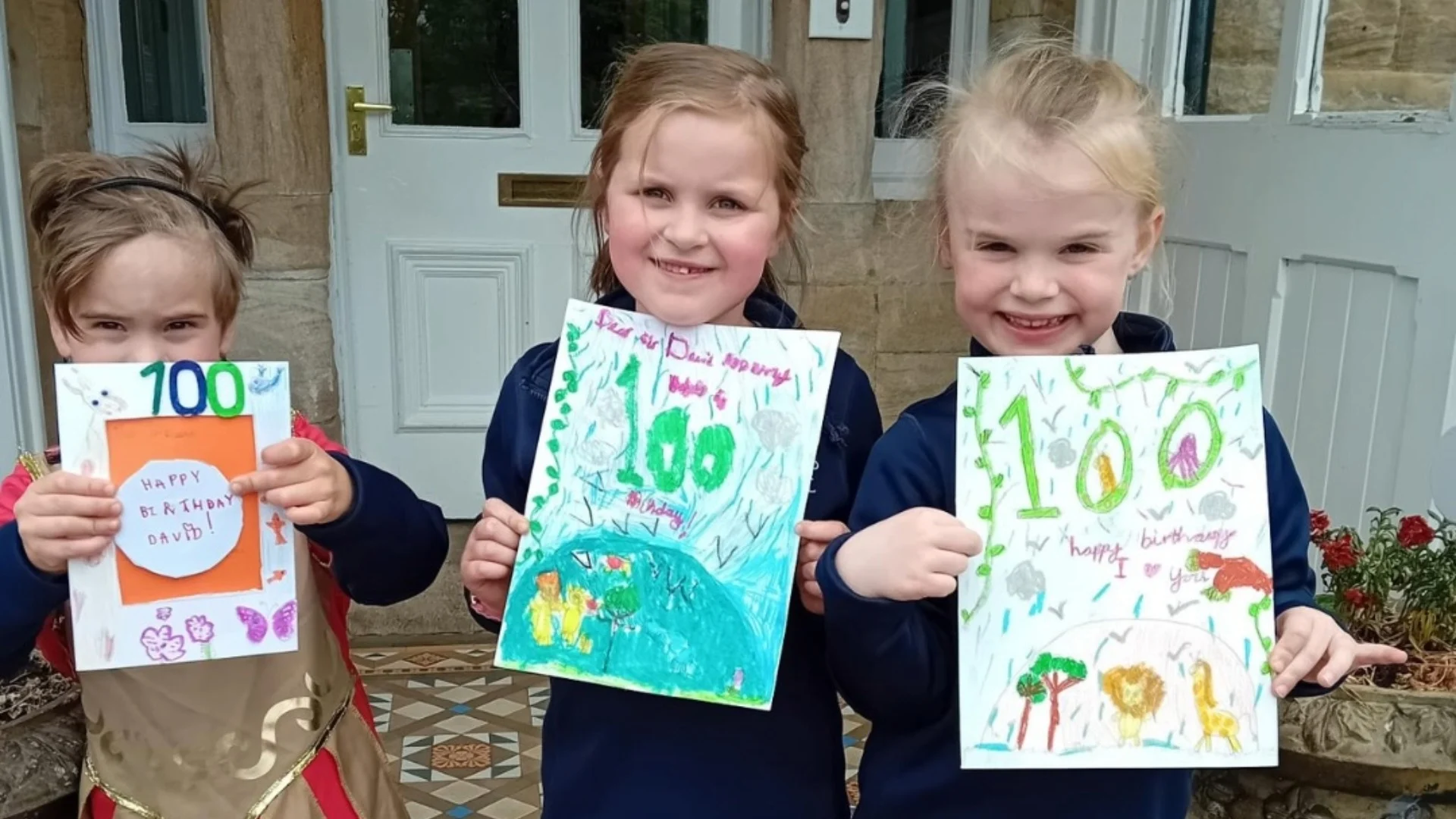 Three Barney pupils showing their hand-made birthday cards for Sir David Attenborough's 100th birthday.