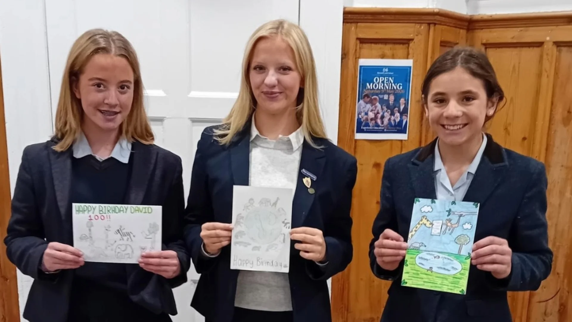 Three Barney pupils showing their hand-made birthday cards for Sir David Attenborough's 100th birthday.