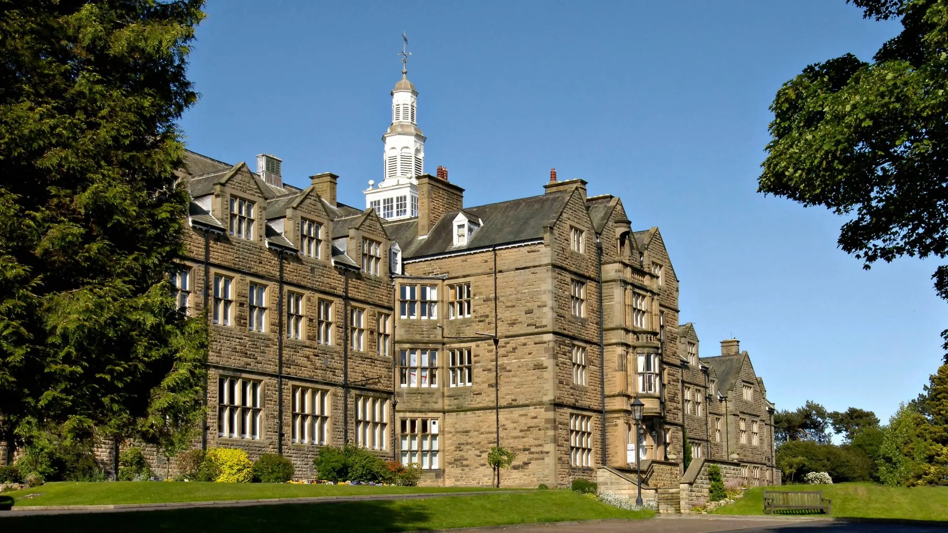 The front of Barnard Castle School nestled between trees on a clear, bright, cloudless day.