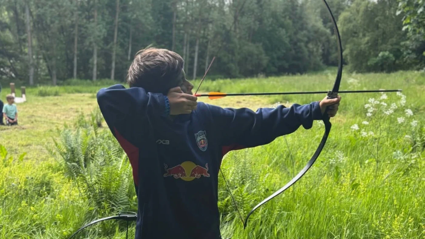 A Barney student shooting a bow in a field.