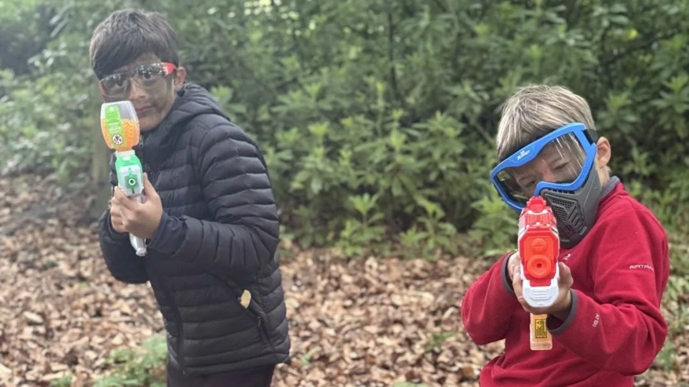 Two Barney Year 5 pupils with Nerf guns in the woods.