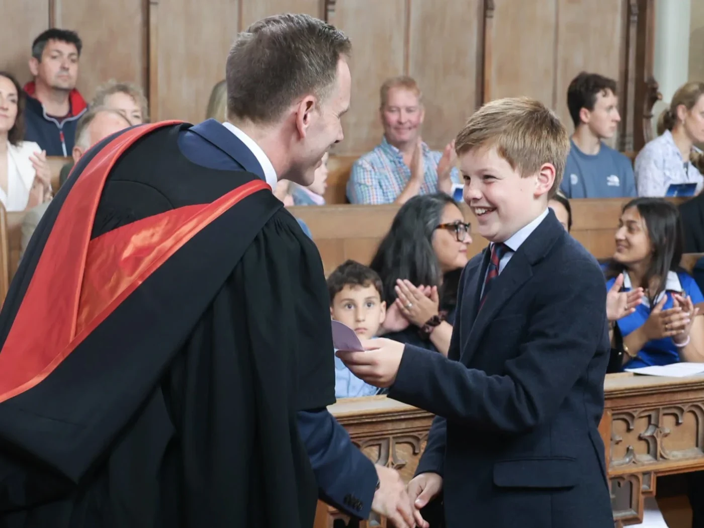 Boy takes envelope from headmaster who is shaking his hand.
