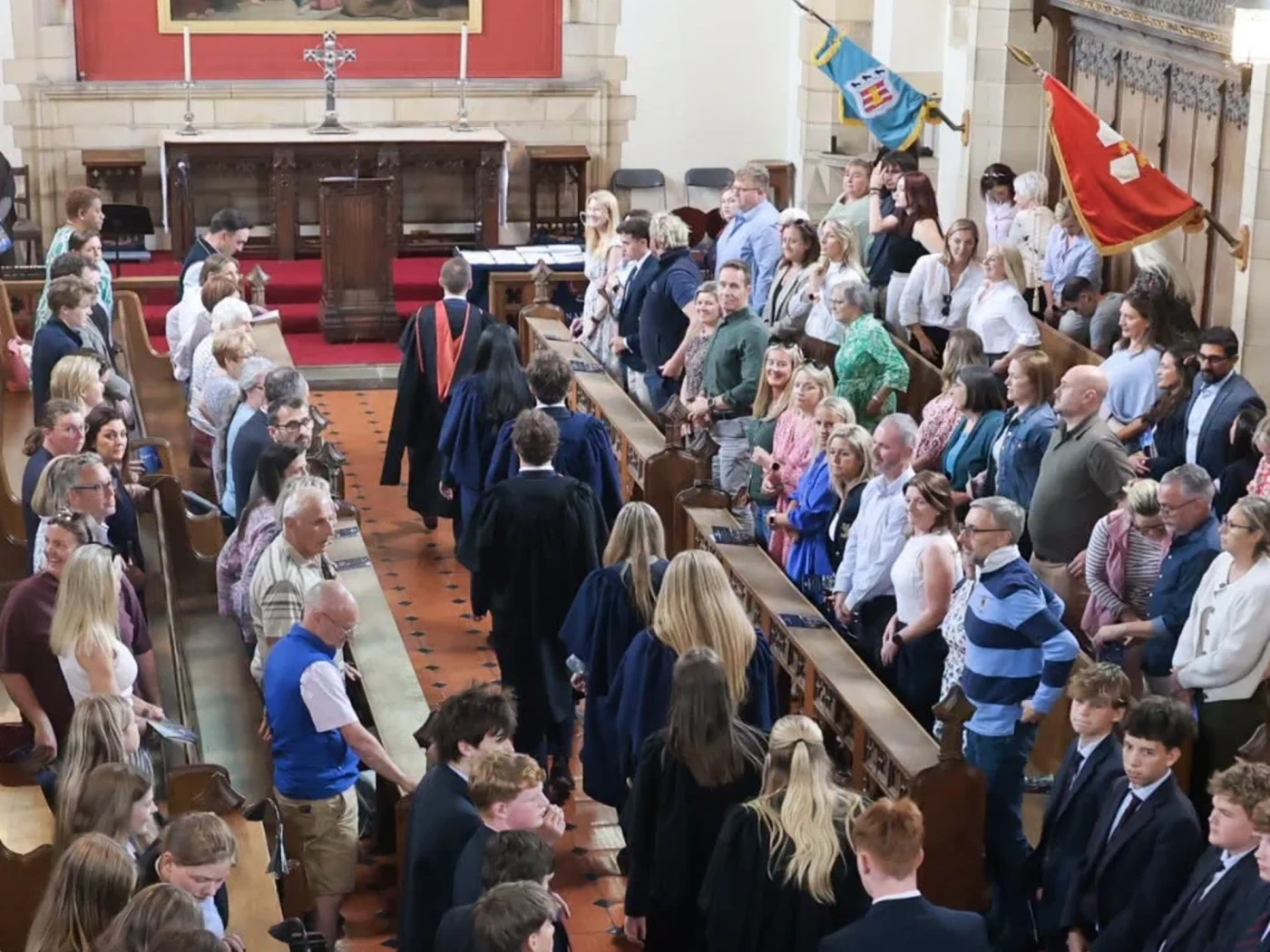 Students follow headmaster down aisle during prize giving ceremony.