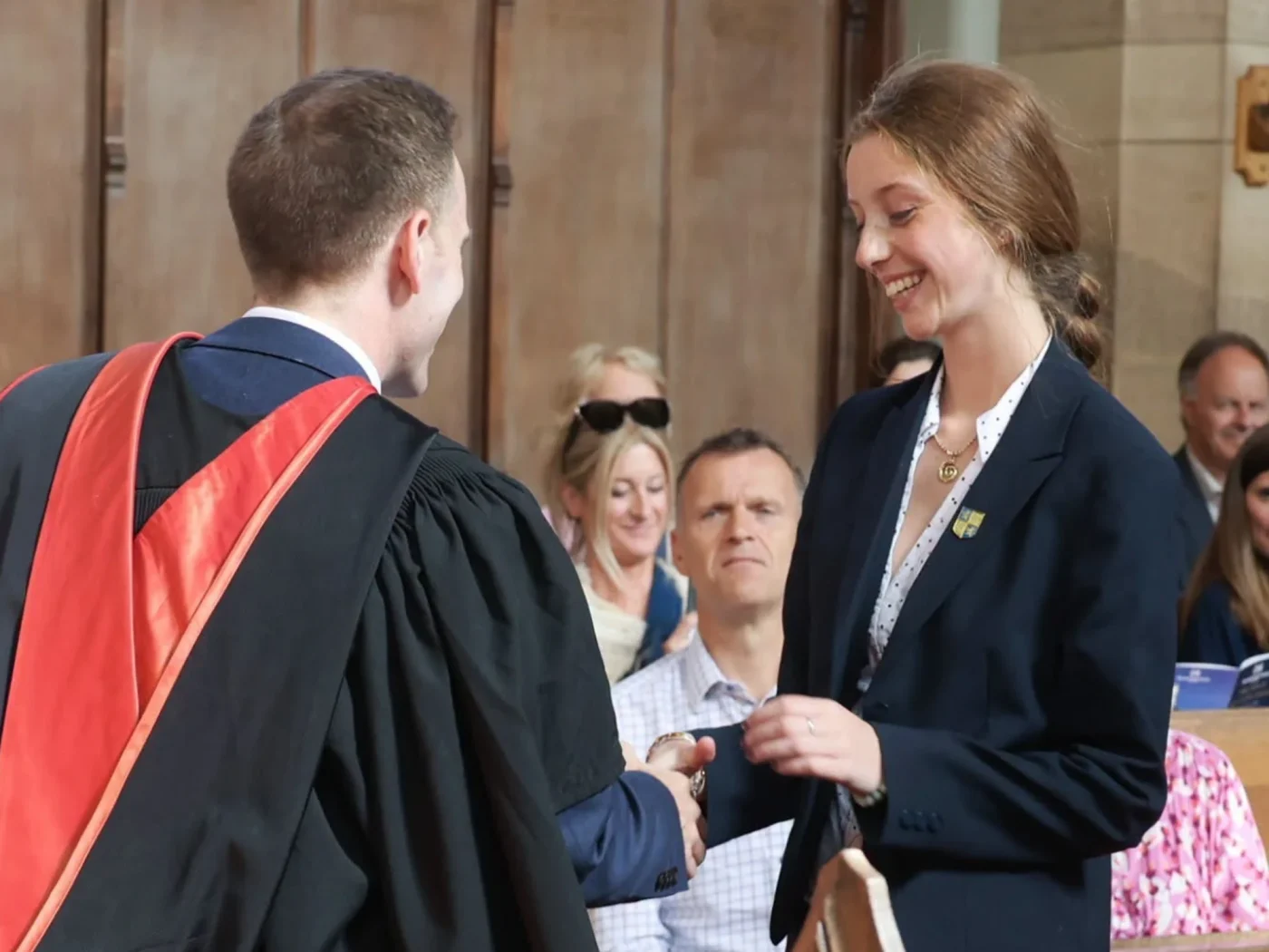 Girl shakes hand with headmaster while receiving a prize during ceremony.