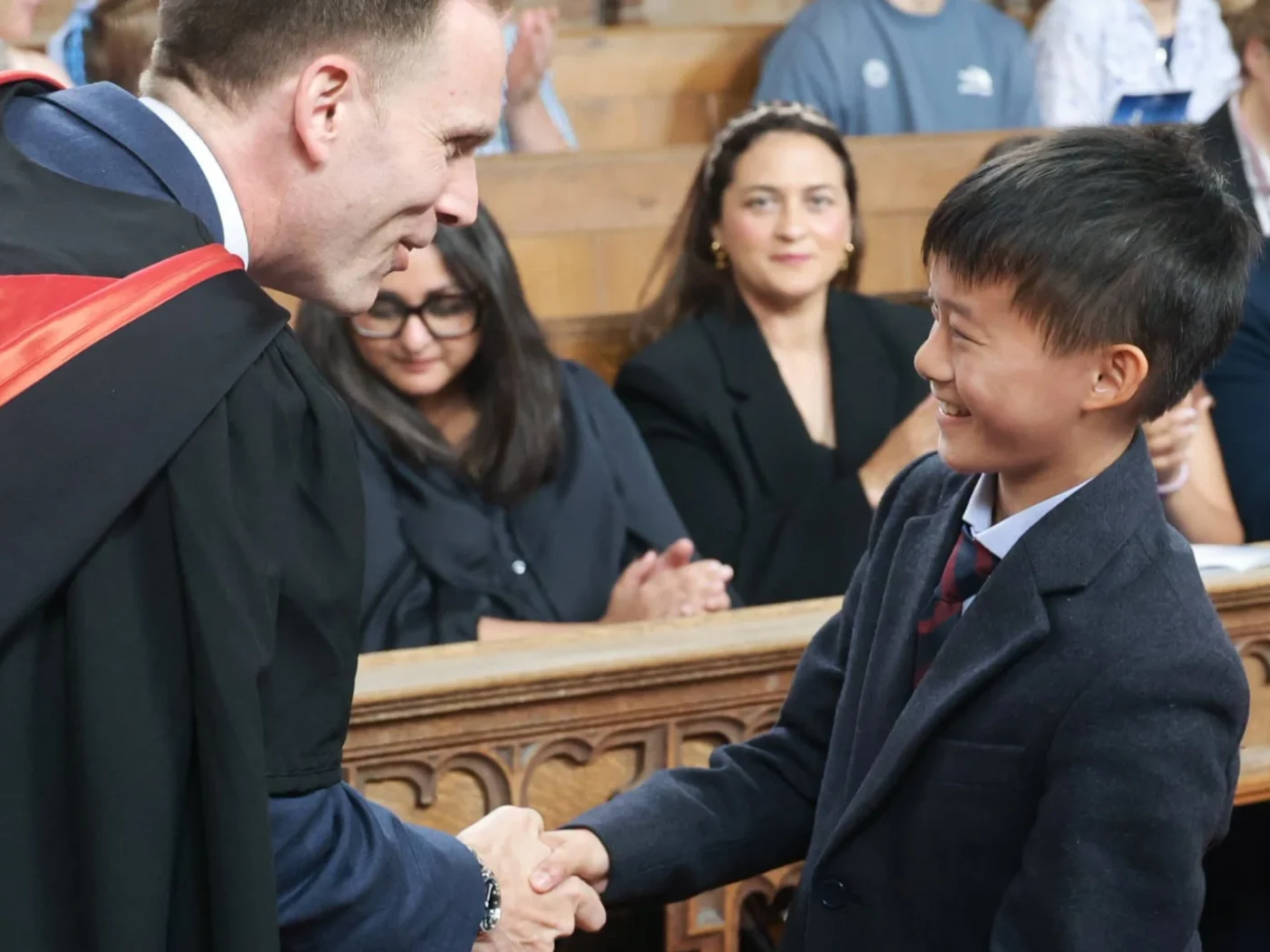 Young boy aged 11-12 smiling and shaking hands with Barnard Castle School Headmaster.