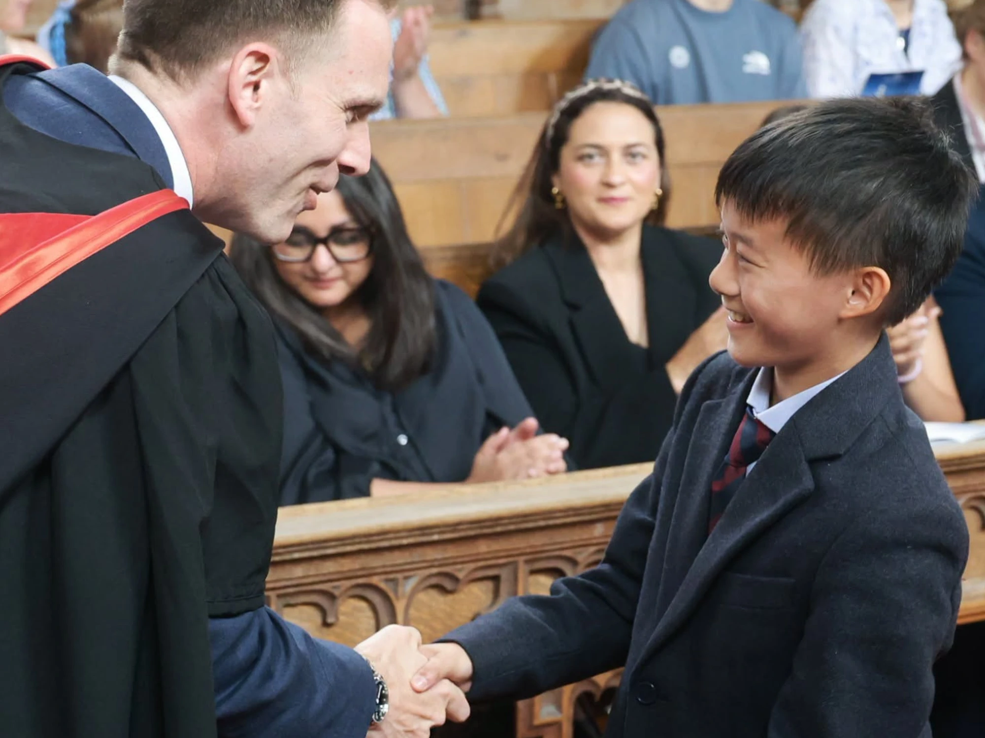 Young boy aged 11-12 smiling and shaking hands with Barnard Castle School Headmaster.