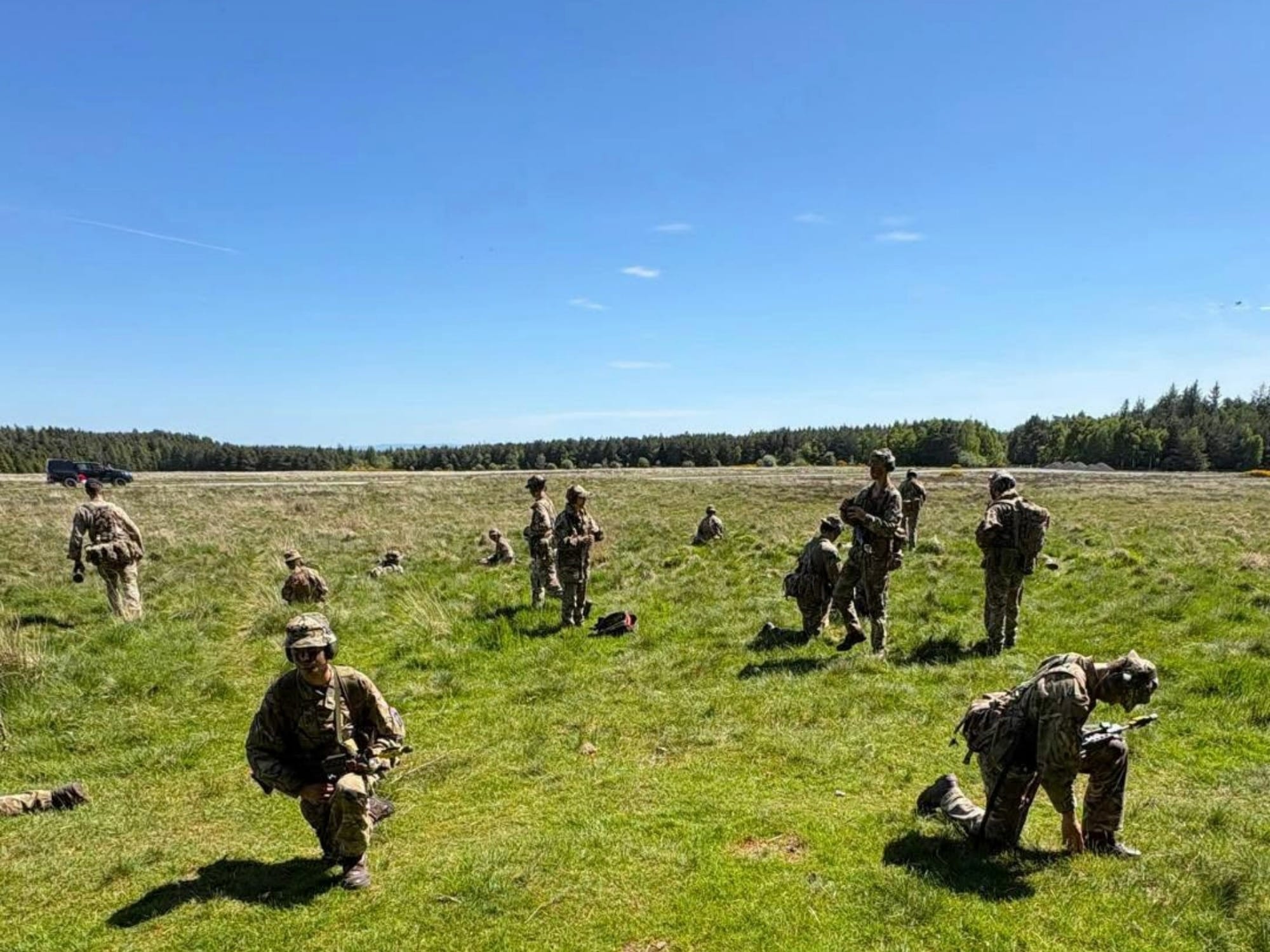 Cadets of the CCF resting during Exercise Battle of Barney on a field under blue skies.