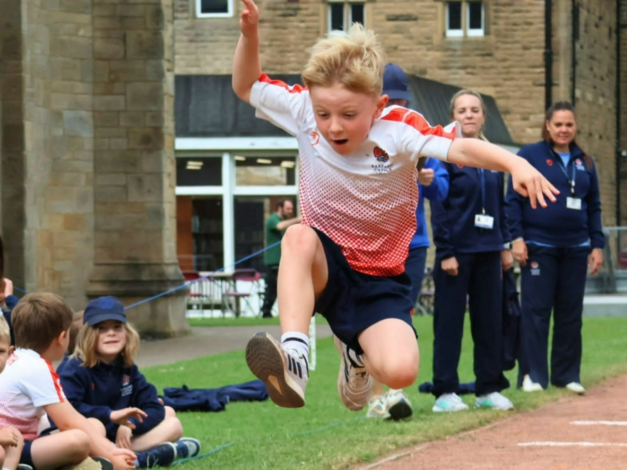 Young Barney pupil mid-air during long jump event on sports day.