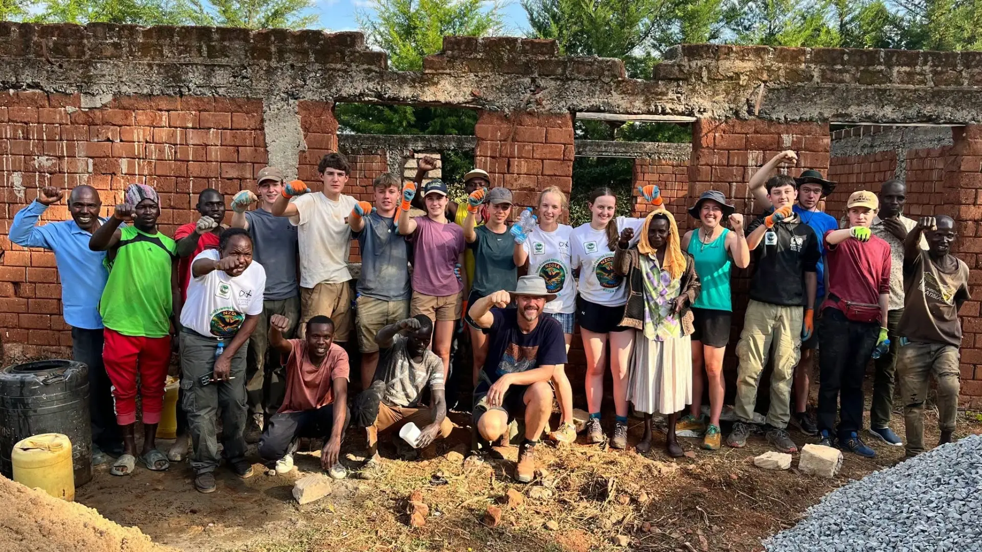 Barney students standing with locals in front of a brick building on the Kenya expedition.