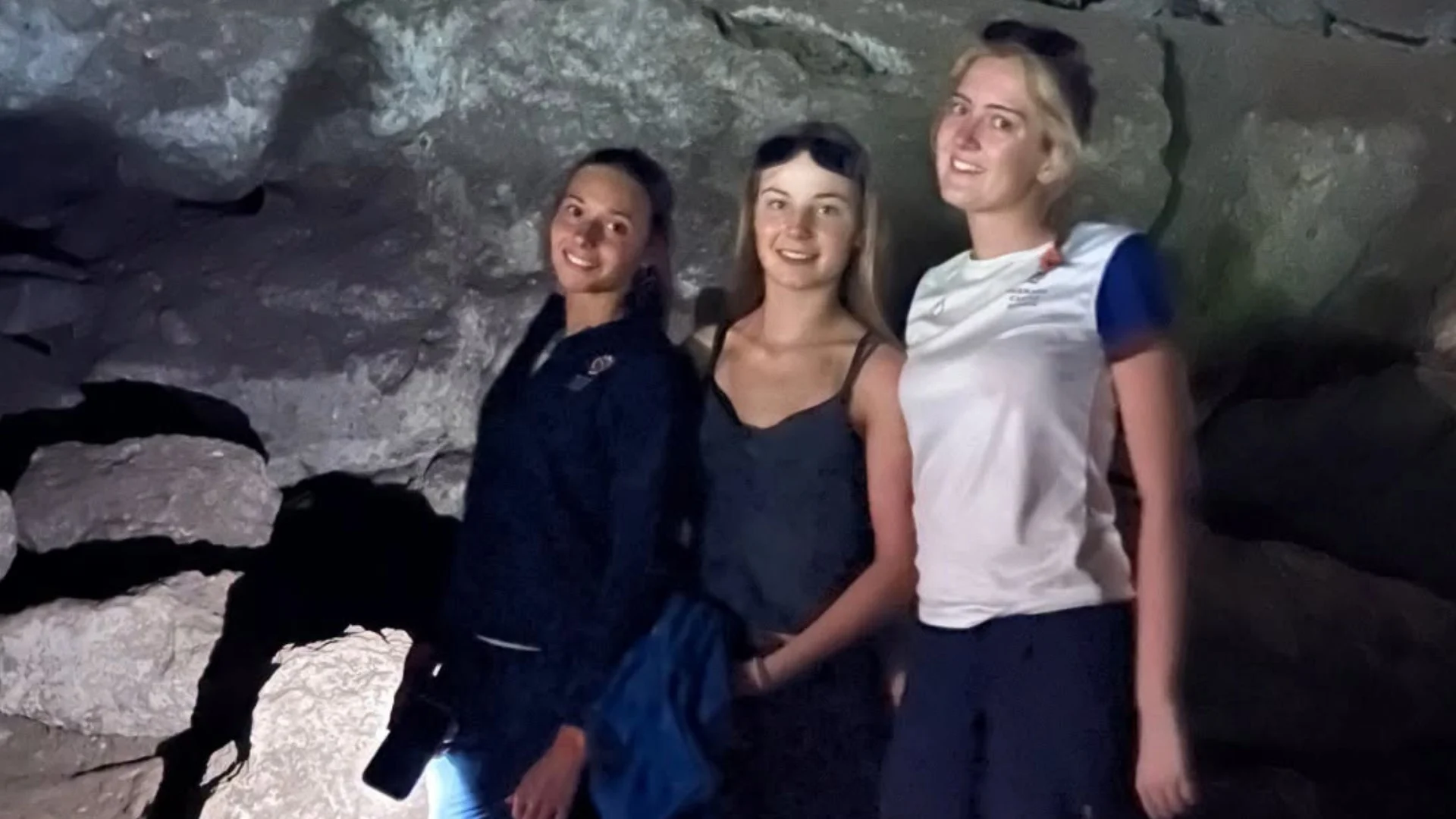 Three Barney students in a large, dark cave.