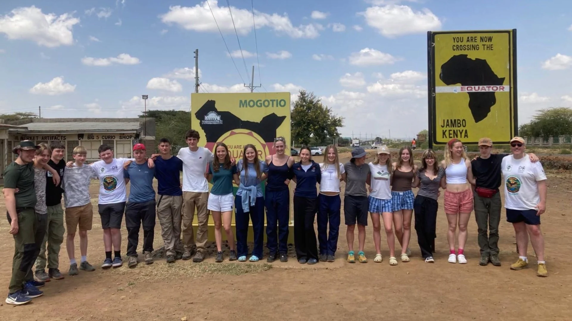 A large group of Barney students in front of road signs marking the equator.