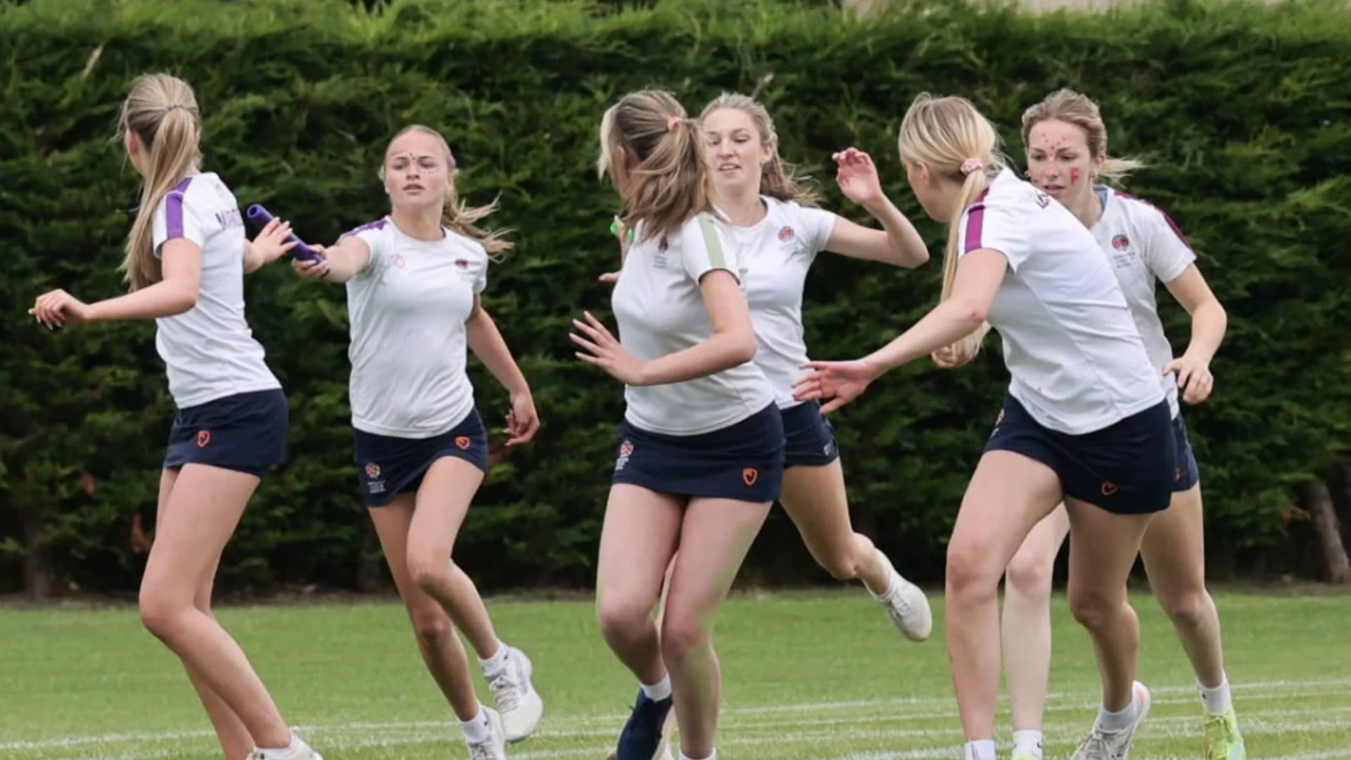 Senior girls passing batons during a race.